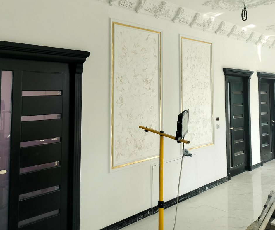 Modern interior hallway with black doors, gold-framed artwork, and a yellow stand.