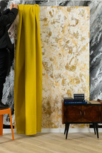 Yellow textured curtain hanging beside a decorative wall with gold and white Venetian stucco finish