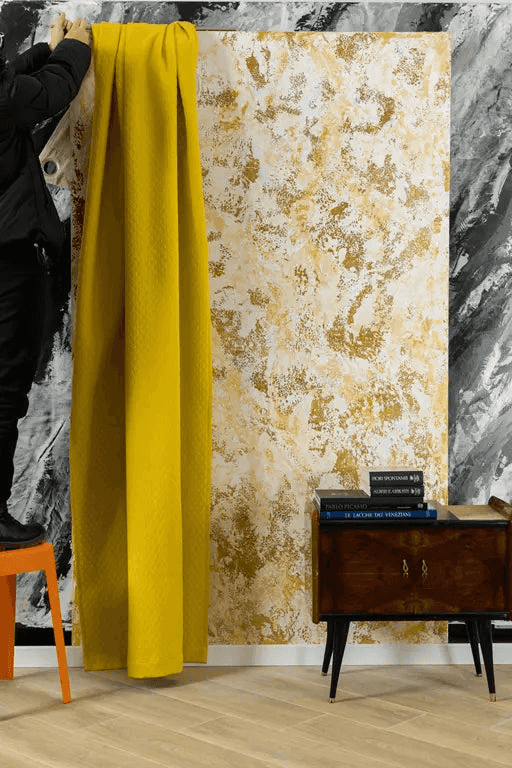 Yellow textured curtain hanging beside a decorative wall with gold and white Venetian stucco finish