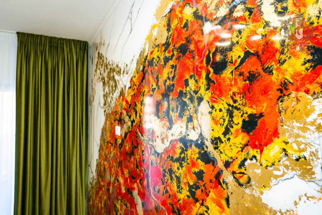 Abstract art with vibrant colors on a wall next to a green curtain.