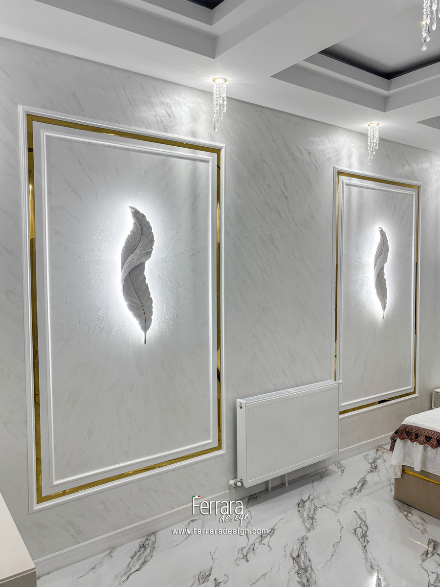 A modern bathroom or spa interior featuring two large illuminated wall art panels with a glowing feather design, gold and white frames, marble-look walls and floor, recessed lighting, and a radiator.