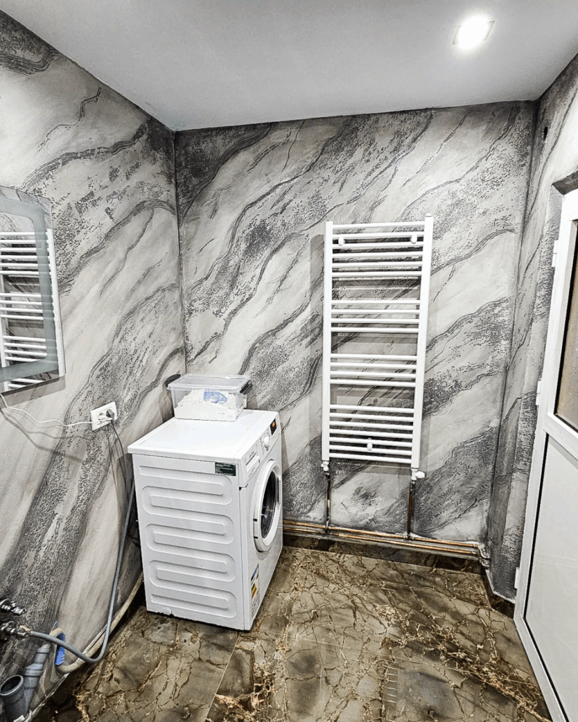 Laundry room with white washing machine, dryer, and towel radiator against marble-patterned walls.