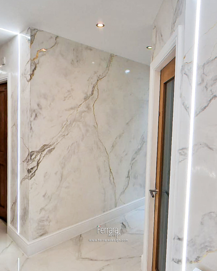 Large white marble wall panels with natural gray and gold veining, installed in a hallway or interior space with white trim and recessed lighting.