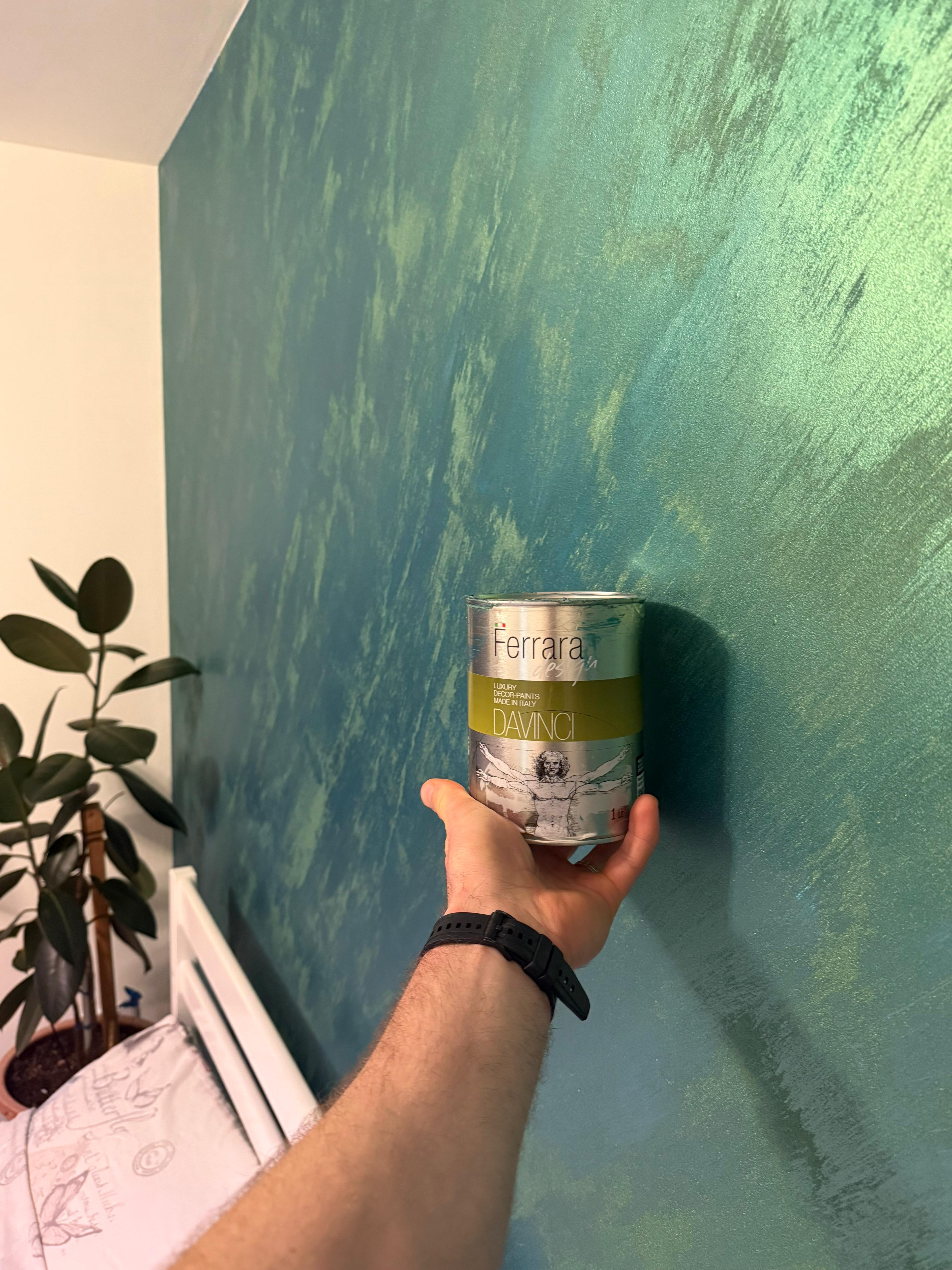 Person holding a can of Ferrari paint against a green wall