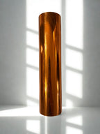 Bronze-colored cylindrical object on a white surface with shadows from vertical blinds.