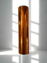 Bronze-colored cylindrical object on a white surface with shadows from vertical blinds.